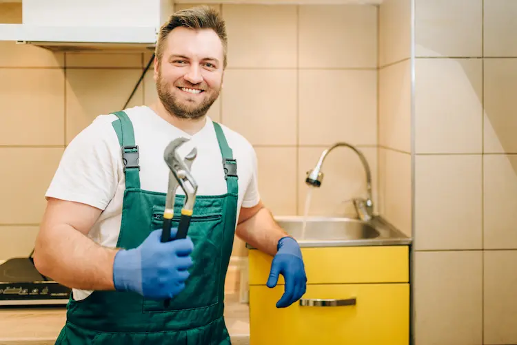 Idraulico sorridente con gli attrezzi in mano in una cucina